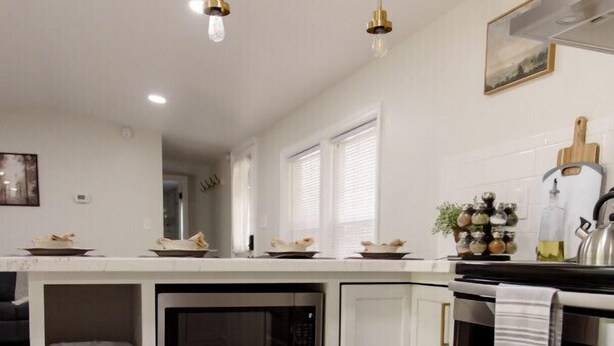 Una cucina moderna con mobili bianchi, un microonde integrato, un forno in acciaio inossidabile e luci a sospensione.