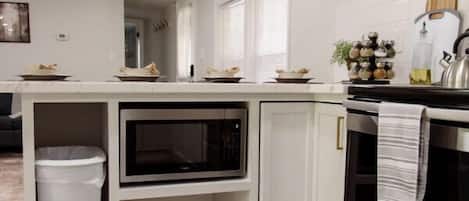 Una cocina moderna con armarios blancos, microondas integrado, horno de acero inoxidable e iluminación colgante.
