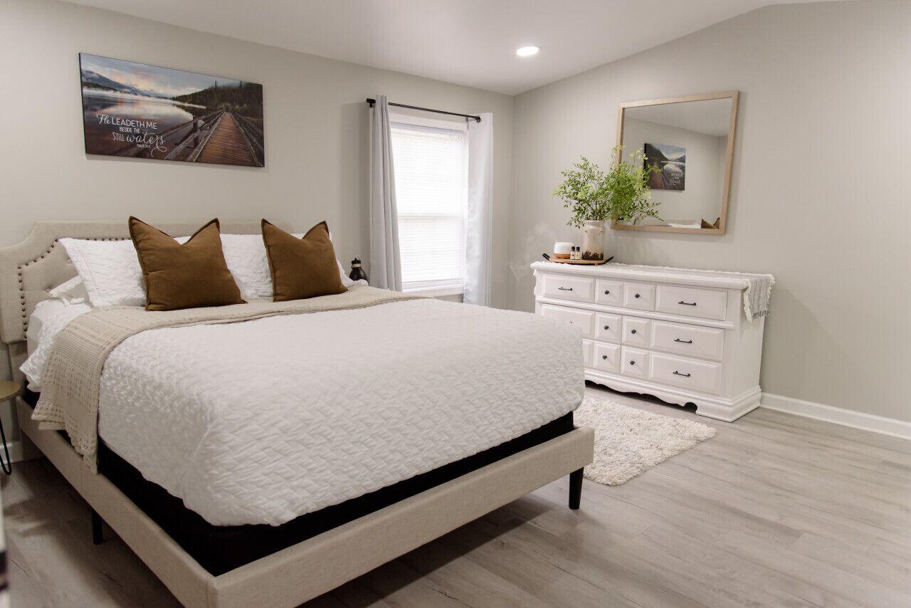 A bedroom with a bed, a dresser, a mirror, and a window with curtains.