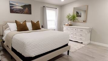 A bedroom with a bed, a dresser, a mirror, and a window with curtains.
