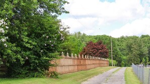 Une allée de gravier mène à une clôture en bois ornée de motifs décoratifs à son sommet.