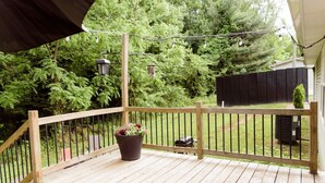 Une terrasse en bois dotée d’une rambarde, entourée de verdure et d’une clôture noire.