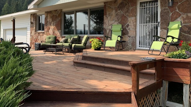 A covered outdoor area with a stone wall, a wooden deck, and two green lounge chairs. - Country Living in Kalispell Montana (Kalispell)