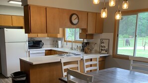 A kitchen with wooden cabinets, a white countertop, a clock, and a window with a view of animals. - Country Living in Kalispell Montana (Kalispell)