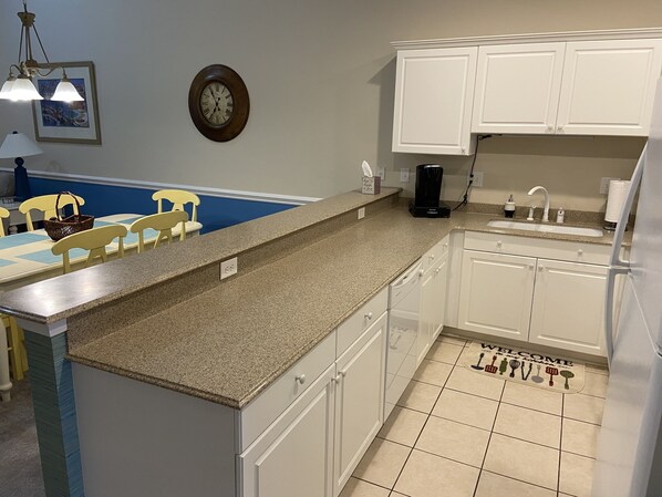 A kitchen with white cabinets, a granite countertop, a coffee maker, and a clock on the wall.