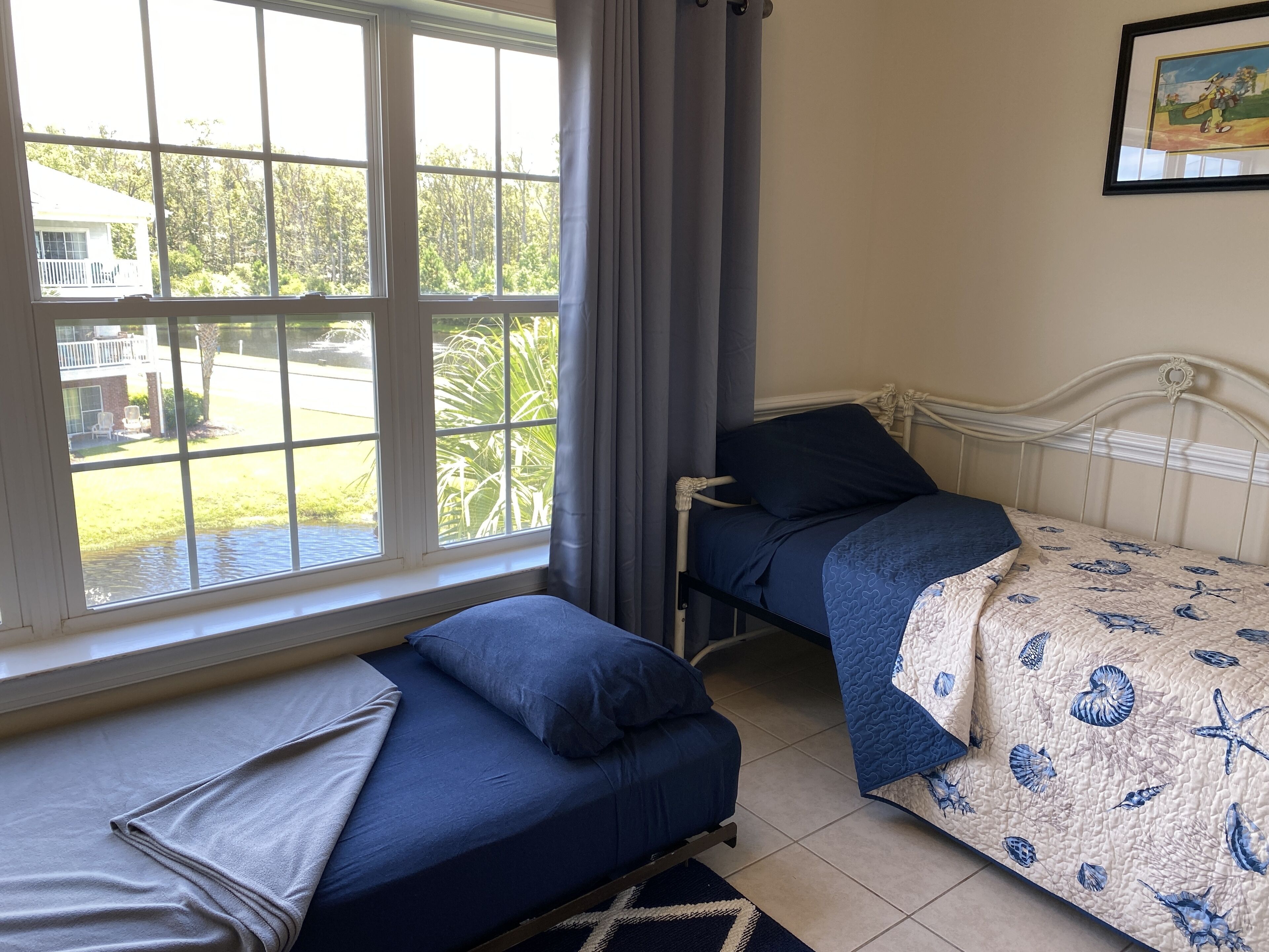 A bedroom with two beds, a large window, and a framed picture on the wall.