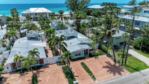 A coastal residential area with houses, palm trees, and a beach in the background.