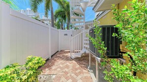 A narrow outdoor corridor with a white gate, a brick floor, and a white fence.
