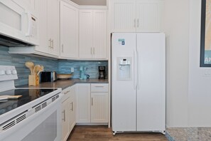Une cuisine avec des meubles blancs, un plan de travail noir, un réfrigérateur blanc et un distributeur d’eau.