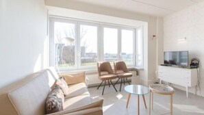 Un salon moderne comprenant un canapé, deux fauteuils, une table basse et un téléviseur posé sur un meuble blanc.