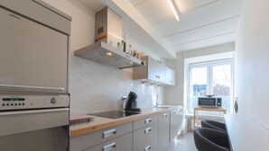 Une cuisine moderne équipée d’un four encastré, d’une machine à café et d’un coin repas avec une chaise noire et une petite table.
