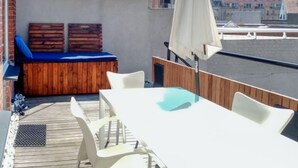 Une terrasse sur le toit avec une plateforme en bois, une table blanche avec des chaises et un coin salon bleu avec des coussins.