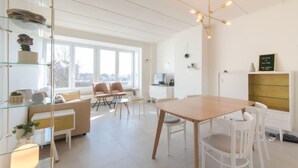 Un salon moderne et bien éclairé, avec un coin repas, de grandes fenêtres et un aménagement minimaliste.