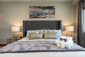 A neatly made bed with a gray headboard, two bedside tables with lamps, and a mountain landscape painting above the bed. - 3 Ski Resorts, Hiking, 2 King Bds, Private Hot Tub (Eden)