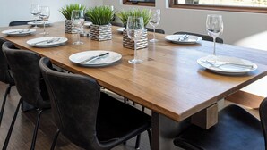En matplats med ett träbord dukat för fyra personer, omgivet av svarta stolar. Det finns krukväxter på bordet och en tavla syns på väggen.