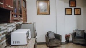 A kitchen with a microwave, cabinets, and a tiled backsplash. There are two armchairs and a small table with a vase of flowers.