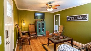 A living room with a wooden floor, a ceiling fan, a television, a cabinet, and a 'WELCOME' sign. - Cozy Getaway with a View! (Trenton)