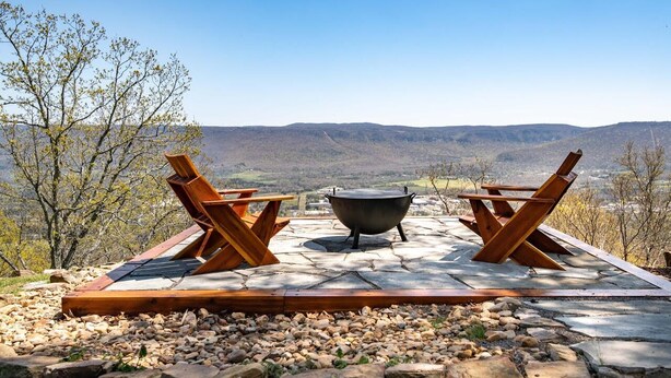An outdoor seating area with two wooden chairs and a large metal pot, set on a stone patio with a view of distant hills. - Cozy Getaway with a View! (Trenton)