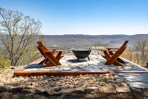An outdoor seating area with two wooden chairs and a large metal pot, set on a stone patio with a view of distant hills.