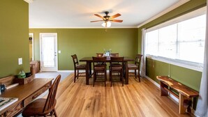 A dining area with a wooden table and chairs, a ceiling fan, and a large window with blinds. - Cozy Getaway with a View! (Trenton)