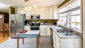 A modern kitchen with white cabinets, stainless steel appliances, a dining area with a table and chairs, and a large window providing natural light. - Cozy Getaway with a View! (Trenton)
