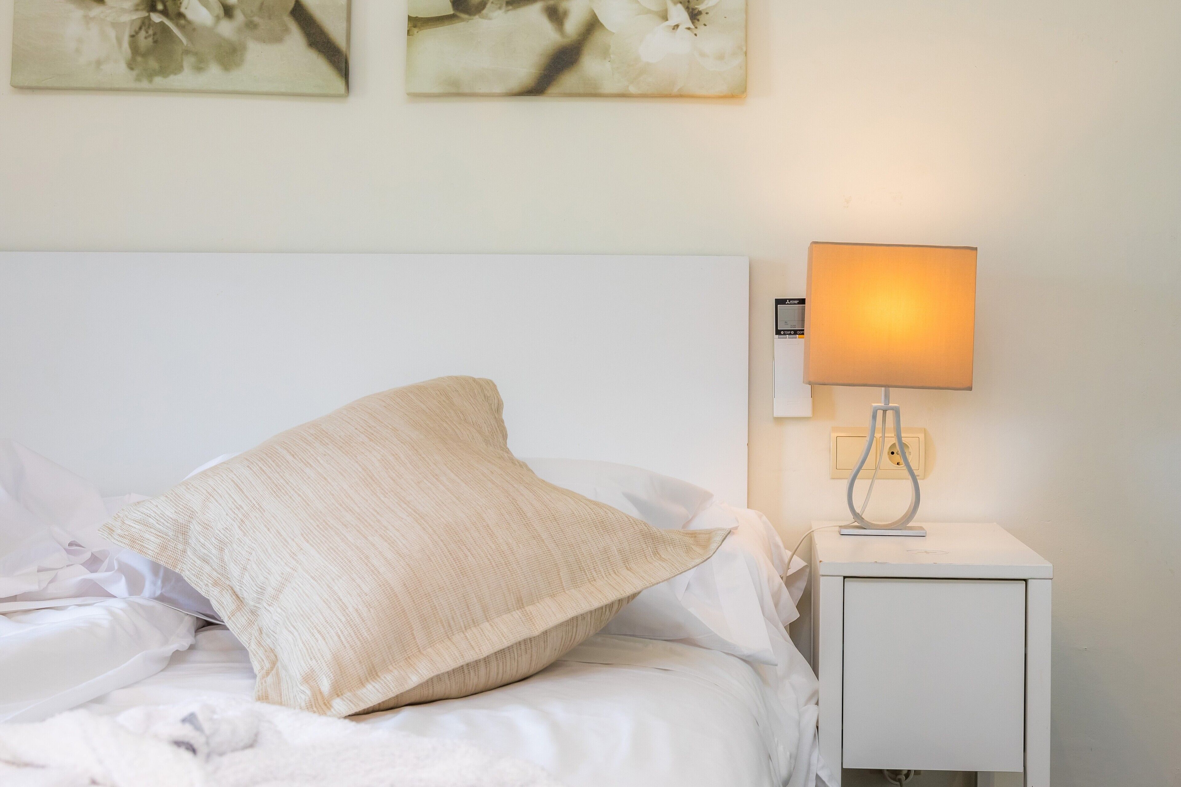 Ein ordentlich bezogenes Bett mit einem Kissen, einer Nachttischlampe und zwei an der Wand befestigten Kunstwerken.