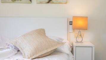 Ein ordentlich bezogenes Bett mit einem Kissen, einer Nachttischlampe und zwei an der Wand befestigten Kunstwerken.