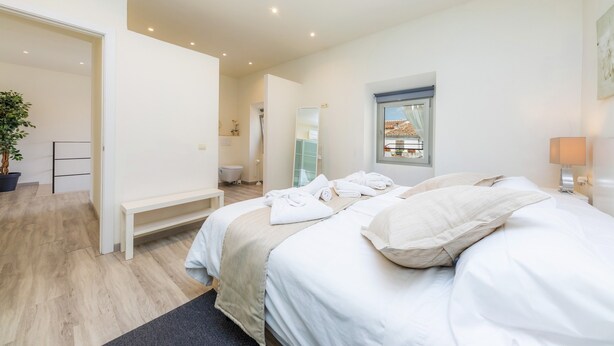A modern hotel room with a large bed, a bedside table, a mirror, and a window.
