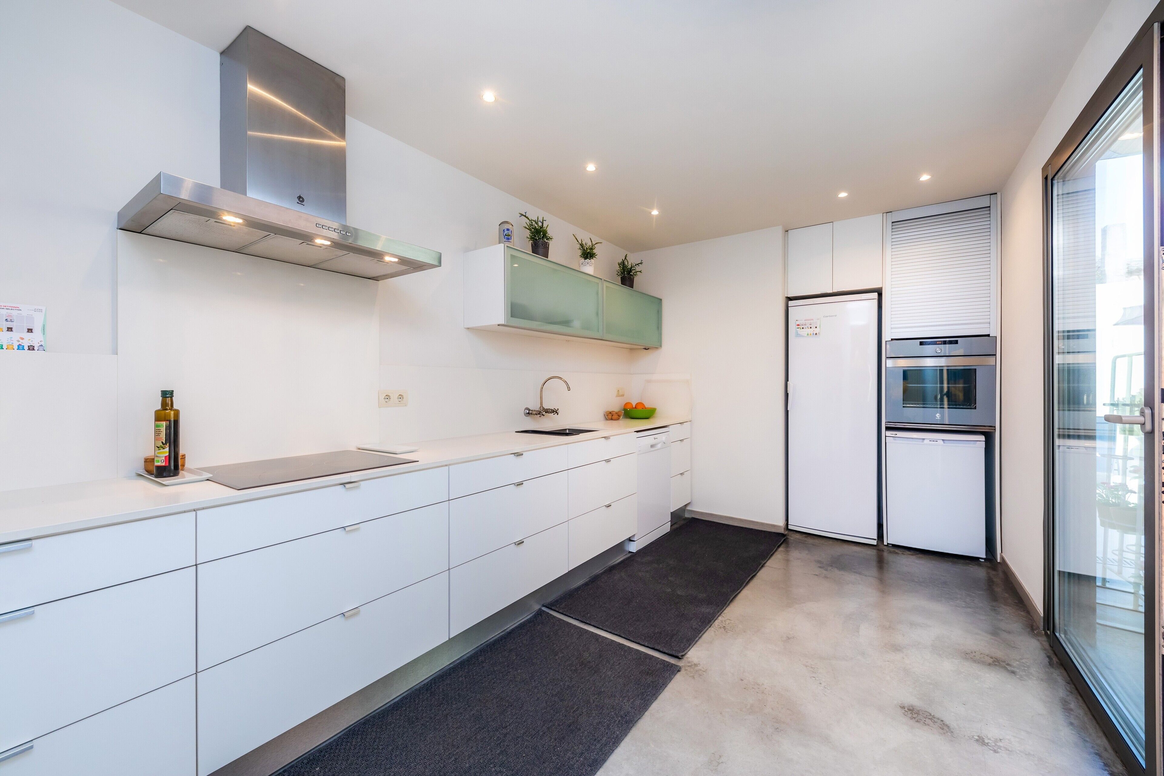 A modern kitchen with white cabinetry, a stainless steel range hood, a built-in oven, and a refrigerator.