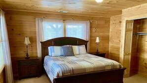 A wooden-paneled bedroom with a large bed, two bedside tables, and a door. - Blue Moon Lodge: Reconnect with Family and Friends with Room to Spread Out! (Clyde)