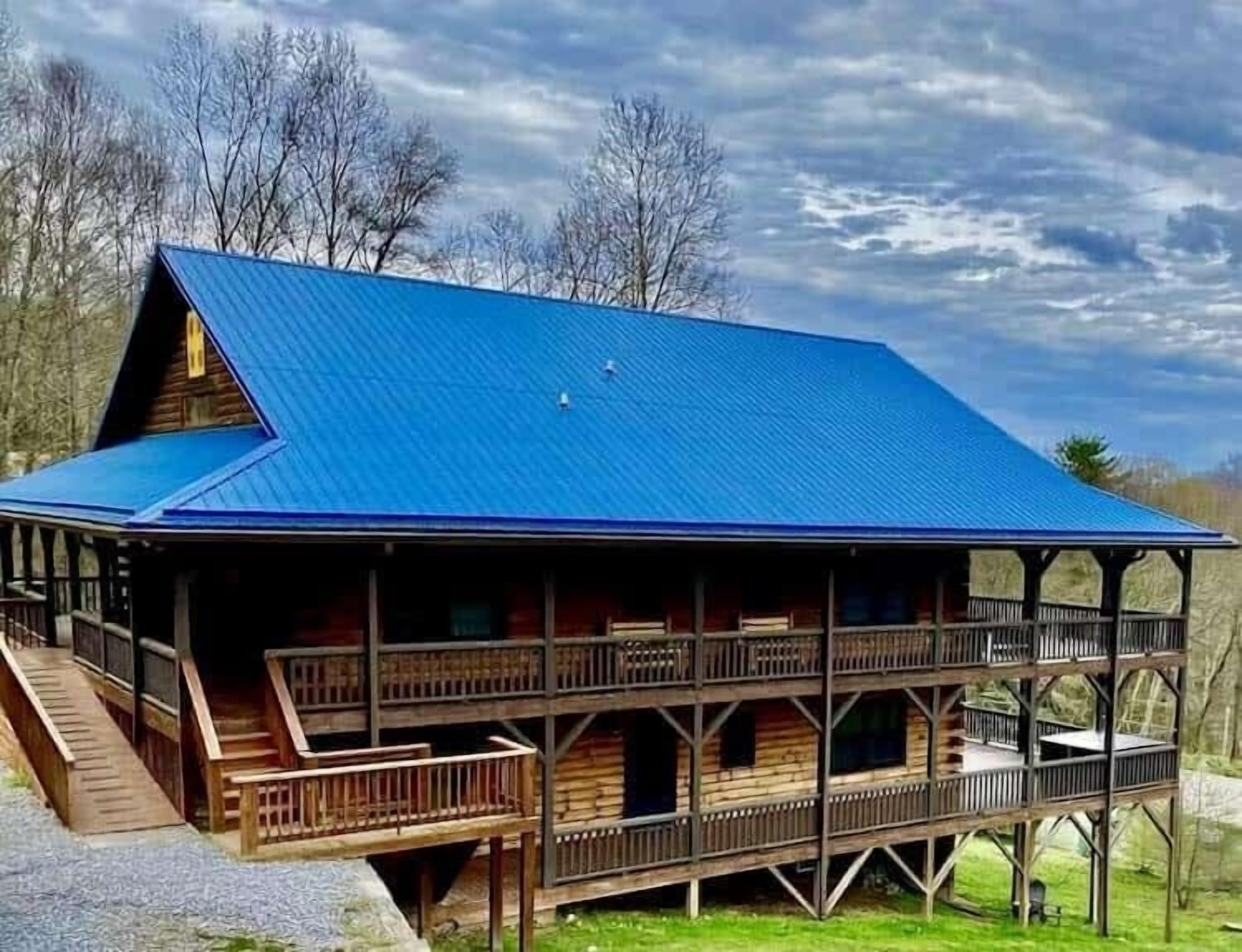 Une cabane avec un toit bleu, un revêtement extérieur en bois et une véranda dotée de balustrades.
