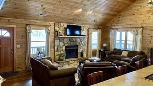 A cozy cabin interior with a stone fireplace, wooden walls, a flat-screen TV, and a dining area. - Blue Moon Lodge: Reconnect with Family and Friends with Room to Spread Out! (Clyde)