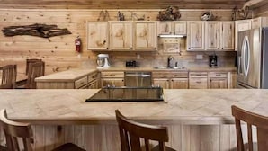 A rustic kitchen with wooden cabinets, a central island, and a stainless steel refrigerator. - Blue Moon Lodge: Reconnect with Family and Friends with Room to Spread Out! (Clyde)