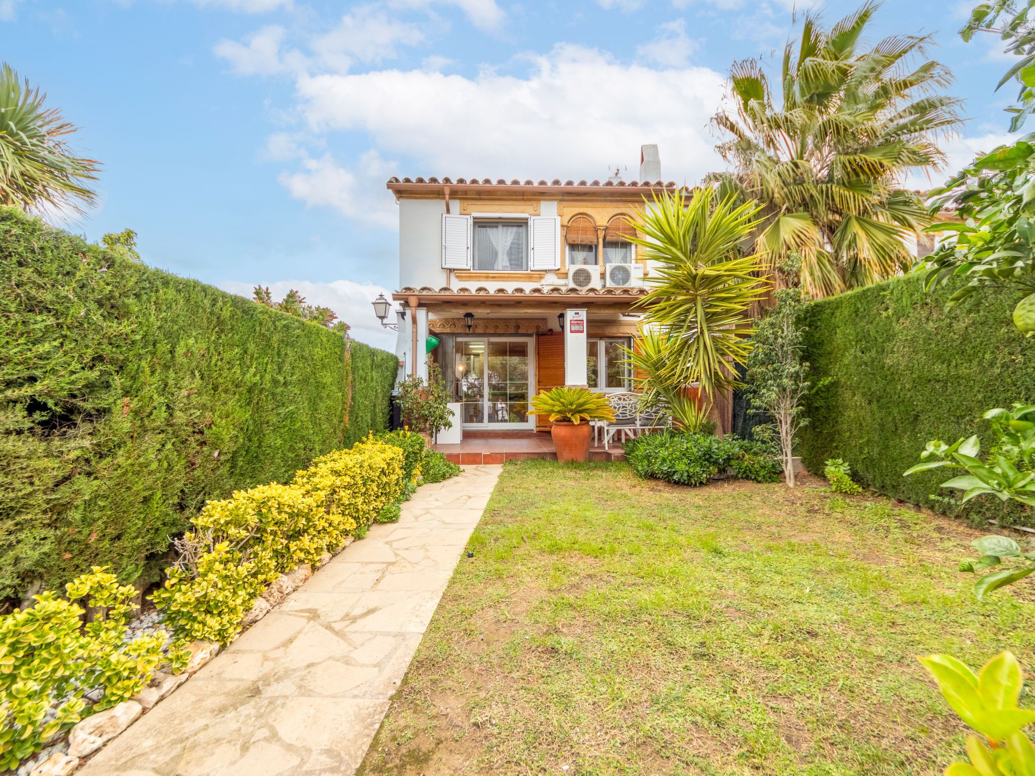 A two-story building with a tiled roof, a front porch with outdoor seating, and a well-maintained garden with a pathway leading to the entrance.