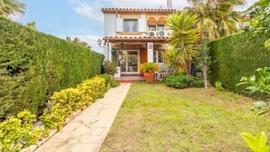 A two-story building with a tiled roof, a front porch with outdoor seating, and a well-maintained garden with a pathway leading to the entrance. - Villa Jardin by Interhome (Cambrils)