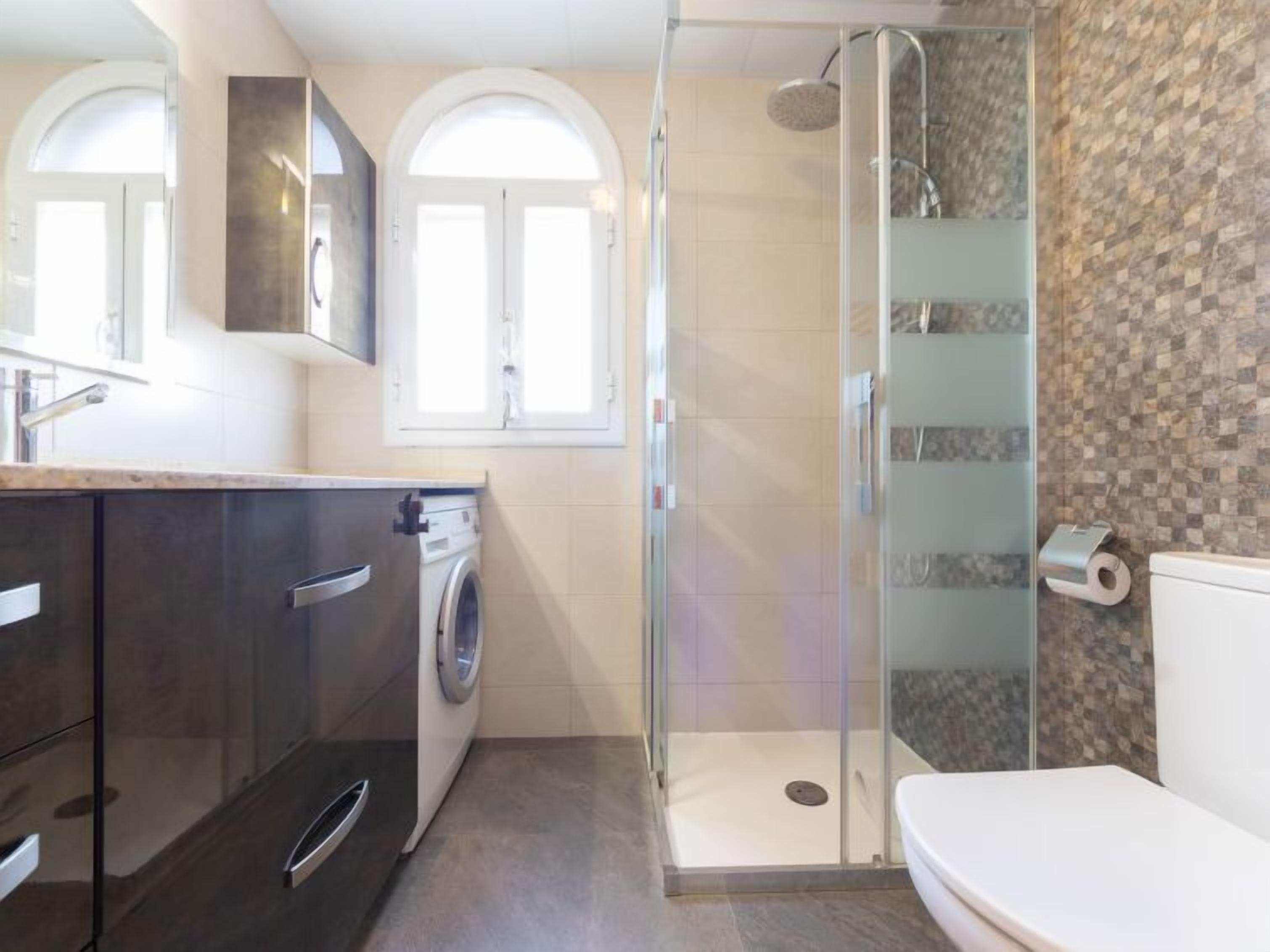 A modern bathroom with a glass-enclosed shower, a washing machine, and a toilet.