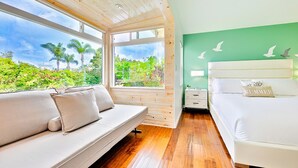 Une chambre avec un plancher en bois, un lit, un canapé et une fenêtre donnant sur un paysage verdoyant.