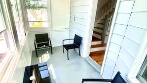 A covered porch with two chairs and a table, a staircase leading to an upper level, and large windows providing views of the outside. - Large 3BR APT w/ enclosed front porch Close to Polar Park, palladium, WPI, DCU  (Worcester)
