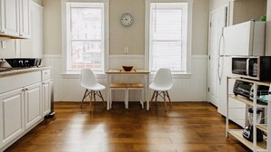 A kitchen with white cabinets, a wooden table, two white chairs, a clock on the wall, and a refrigerator. - Large 3BR APT w/ enclosed front porch Close to Polar Park, palladium, WPI, DCU  (Worcester)