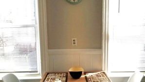 A room with a wooden table, two white chairs, a wall clock, and a window with blinds. - Large 3BR APT w/ enclosed front porch Close to Polar Park, palladium, WPI, DCU  (Worcester)
