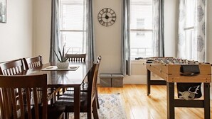 A dining area with a wooden table and chairs, a foosball table, and a wall clock. - Large 3BR APT w/ enclosed front porch Close to Polar Park, palladium, WPI, DCU  (Worcester)