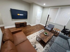 Un salon comprenant un téléviseur à écran plat, un canapé marron, un fauteuil gris, une table basse et une petite table d’appoint.