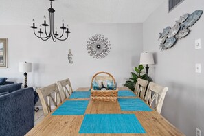 Un coin repas avec une table en bois, des sets de table bleus, un centre de table en osier et des œuvres d'art décoratives accrochées au mur.