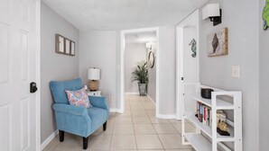 Un pasillo con un sillón azul, una estantería blanca y una planta en maceta.