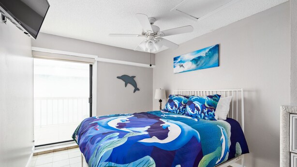 Un dormitorio con cama, ventilador de techo, pintura de delfín y vista al océano a través de la puerta corrediza.