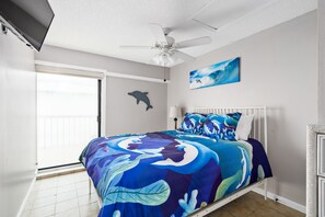 A bedroom with a bed, a ceiling fan, a painting of a dolphin, and a view of the ocean through the sliding door. - 4 BR Oasis, water views every room steps to beach! (Clearwater)