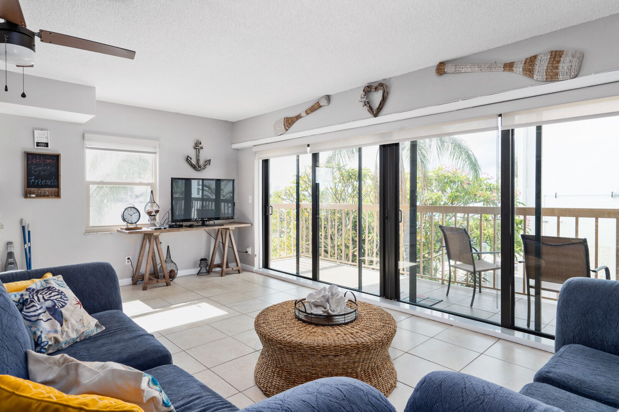 A spacious living area with a large sliding glass door leading to a balcony, a comfortable sofa, a television, and a small table with decorative items.
