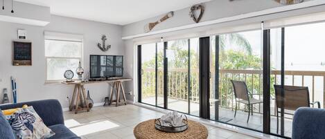 Un vaste espace de vie comprenant une grande porte-fenêtre coulissante donnant sur un balcon, un canapé confortable, un téléviseur et une petite table agrémentée d’objets décoratifs.