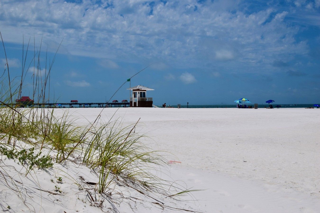 Ein Strand mit einem Rettungsturm, einer Mole und Strandsonnenschirmen.