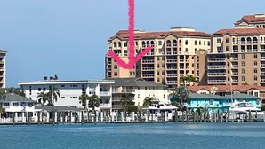 Un hotel frente a la playa con varios balcones, un puerto deportivo y un cielo azul despejado.